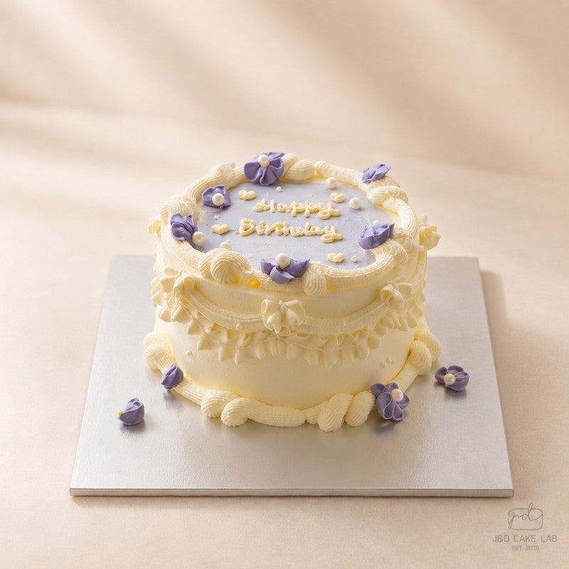 Side view of a lilac vintage cake with layered cream piping, purple flowers and pearl details
