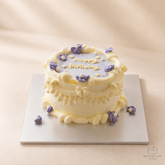 Side view of a lilac vintage cake with layered cream piping, purple flowers and pearl details