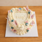 Front view of a vintage heart-shaped gender reveal cake with detailed cream piping and butterfly decorations