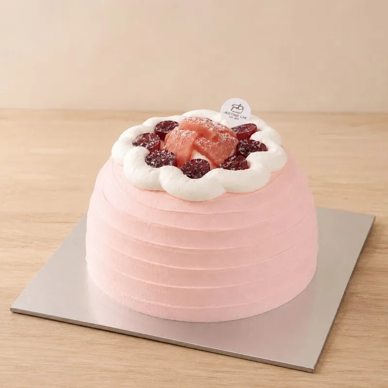 High-angle view of a blush guava cream cake topped with red grapes, guava pieces and white cream