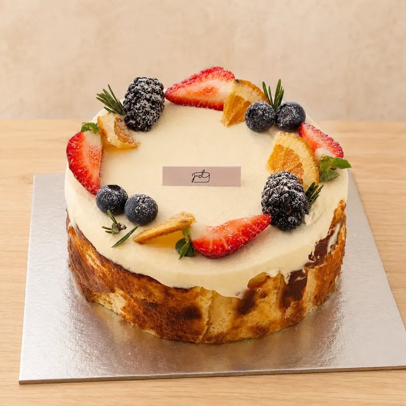 Three-quarter view of creamy Basque burnt cheesecake decorated with strawberries, berries and citrus
