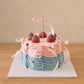 Three-quarter view of pastel birthday cake with layered pink and blue ruffles and ribbon bows