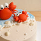 Handmade small fondant crab with seashell and pearl details on a seaside birthday cake