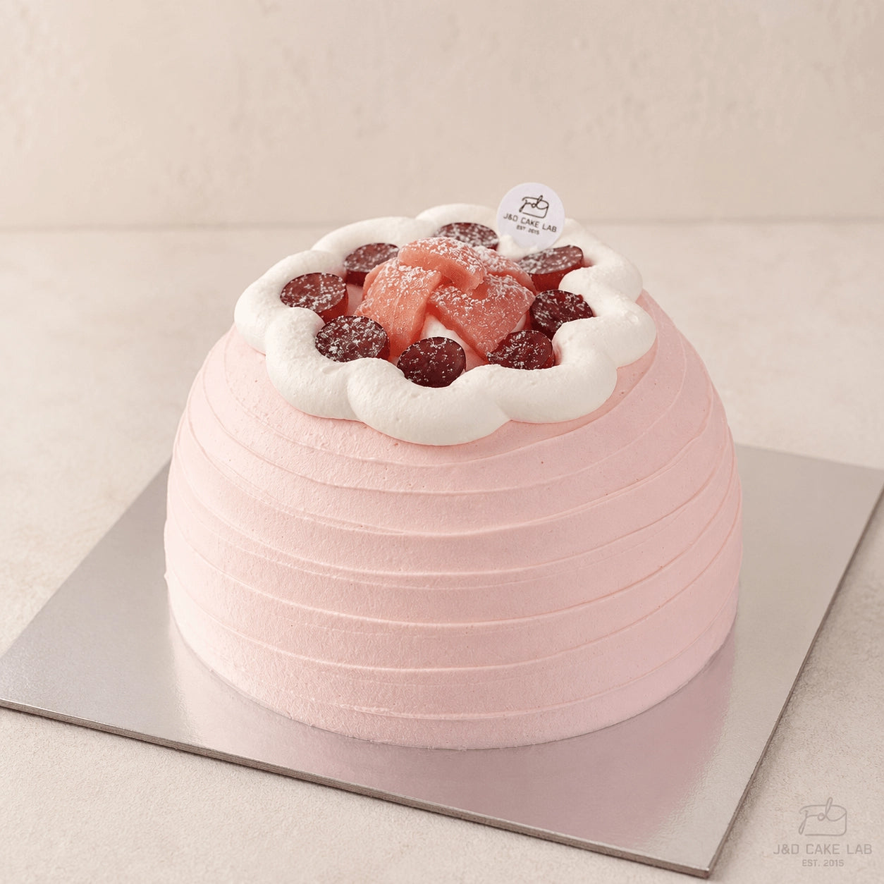 Front view of a pink guava cream cake with horizontal texture and red grape topping