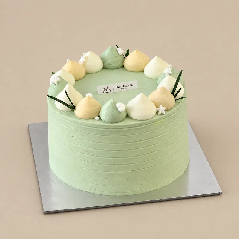 Pale green lychee and green tea cake with pastel cream dollops, small white flowers and green leaf decorations.