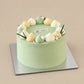 Pale green lychee and green tea cake with pastel cream dollops, small white flowers and green leaf decorations.