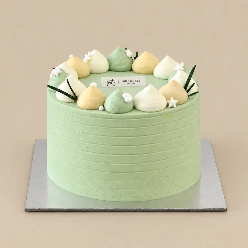 Front view of Lychee Green Tea Cloud cake with fine horizontal cream detailing on a square silver board.

