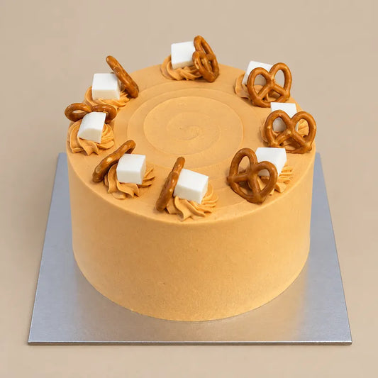 Thai Tea Velvet cake with orange cream, piped swirls, white cubes and golden pretzels on a silver cake board.