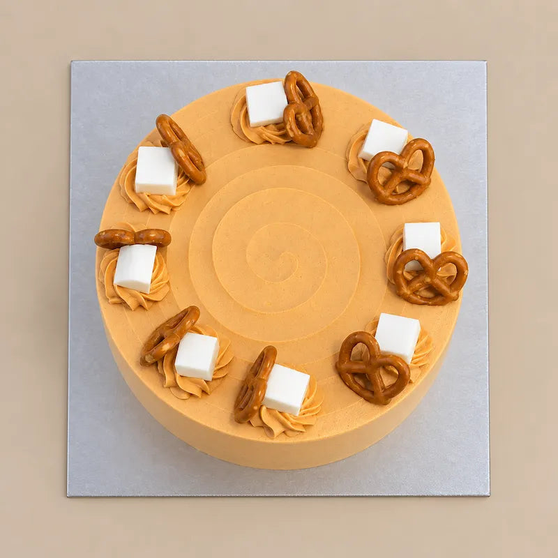 Top view of Thai Tea Velvet cake with a spiral cream finish surrounded by piped swirls, white cubes and pretzels.