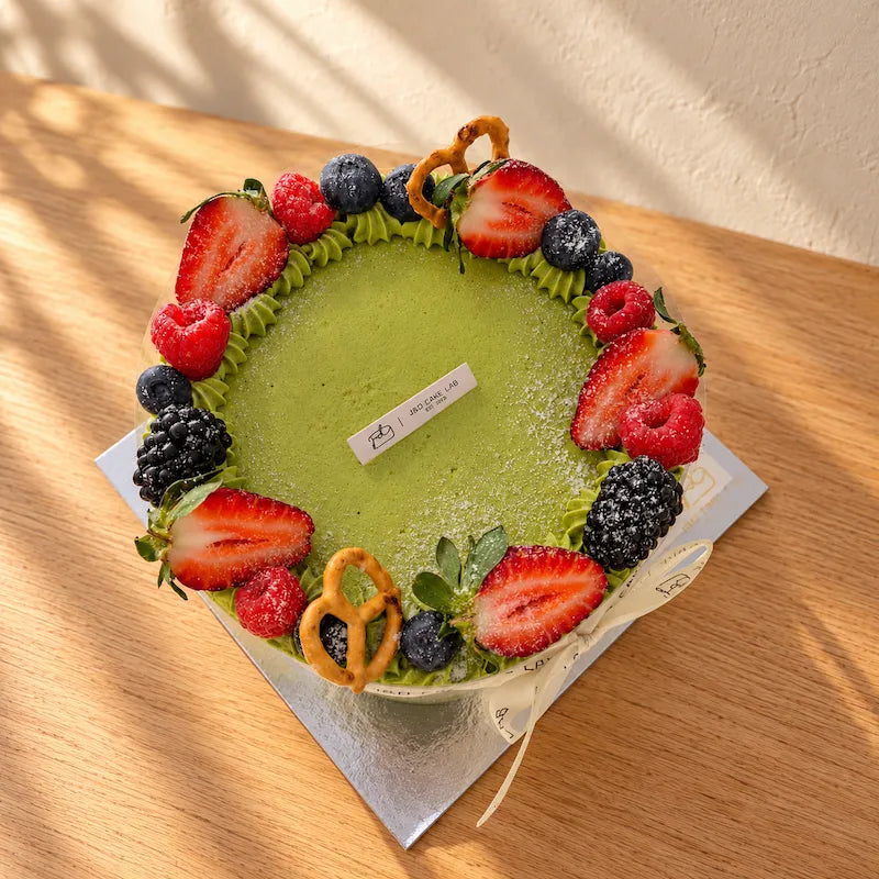 Top view of a Uji matcha cream cake with a green piped border, strawberries, blueberries, raspberries and blackberries.